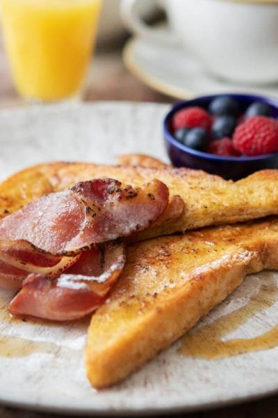 Slices of toast with bacon rashers drizzled with maple syrup, accompanied by berries