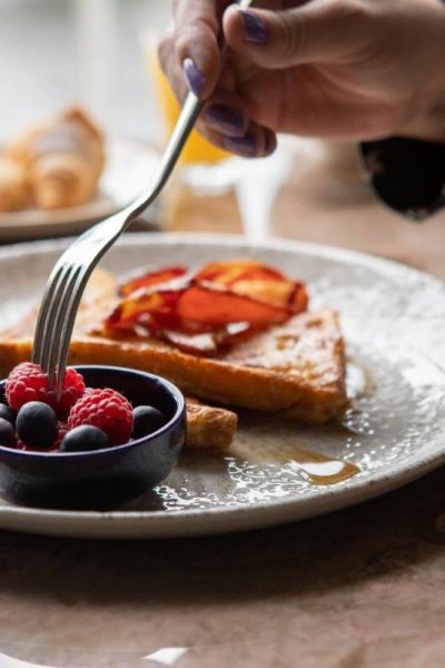 Fork picking berries from a plate of toast and bacon drizzled with maple syrup